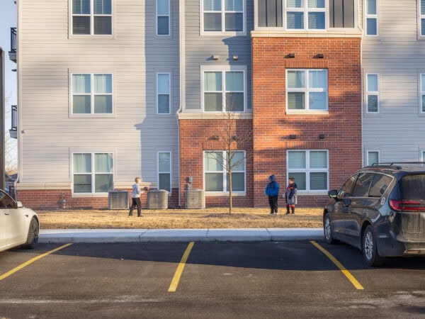 Modern apartment building with parking lot and residents outside.