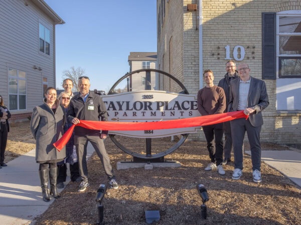 Group unveiling new Taylor Place Apartments sign outside building.