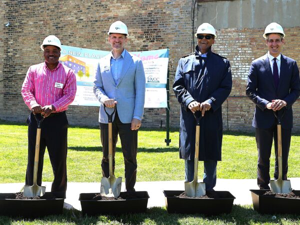 8 professionally dressed men and women wearing white hard hats pose with shovels for a groundbreaking ceremony. They smile, conveying a sense of accomplishment and teamwork.