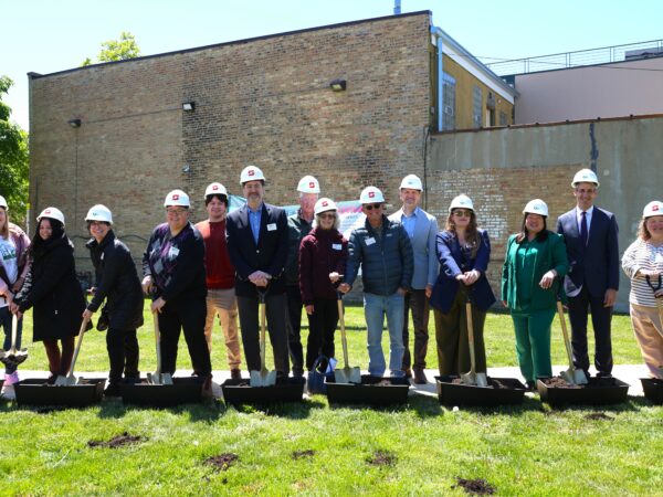 A group of people wearing hard hats pose with shovels at a groundbreaking event.