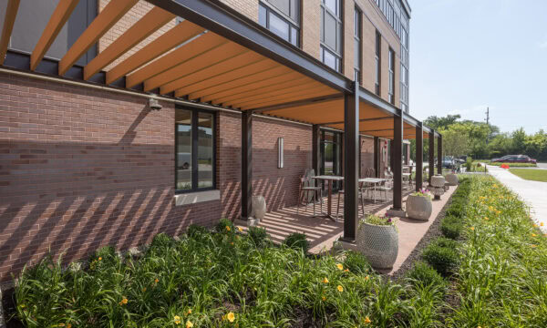 Exterior of a four story apartment building with a covered patio and attractive landscaping with yellow flowers in front.