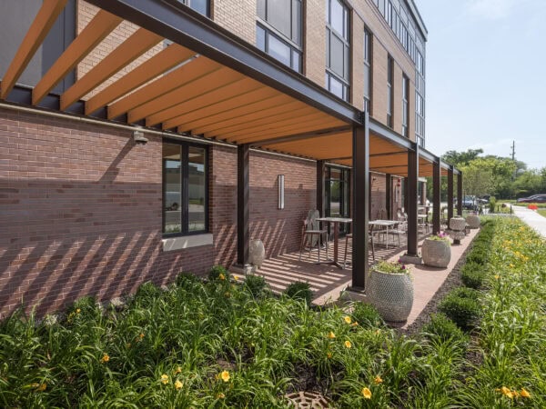 Exterior of a four story apartment building with a covered patio and attractive landscaping with yellow flowers in front.