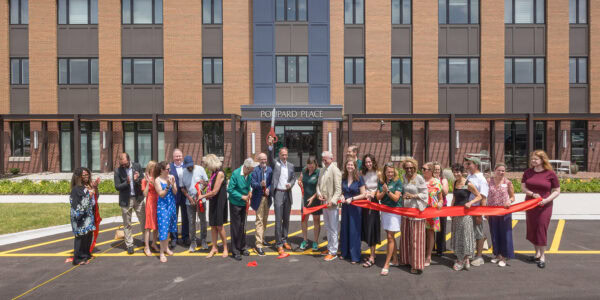 People holding a red ribbon that has just been cut, standing in front of a beautiful apartment building.