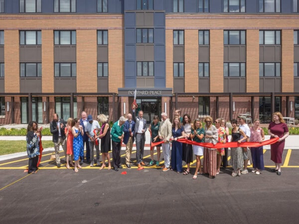 People holding a red ribbon that has just been cut, standing in front of a beautiful apartment building.
