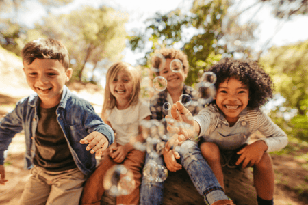 A group of kids laugh and play with bubbles.