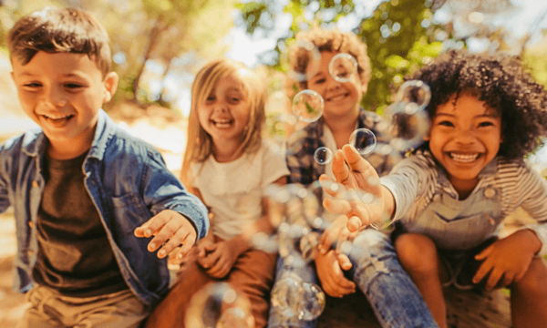 A group of kids laugh and play with bubbles.