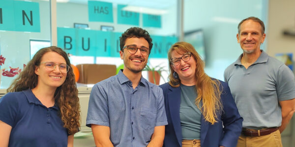 Group of four diverse professionals smiling in modern office environment.