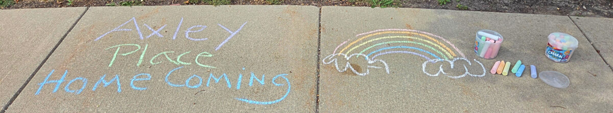 Chalk drawings on the sidewalk that say Axley HomeComing and a rainbow. Sidewalk chalks lay on the side.